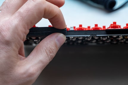 Si può vedere il tappetino isolante tra la piastra di copertura e la scheda. Con le dita schiaccio le guarnizioni che danno alla tastiera la sua sensazione di digitazione flessibile.